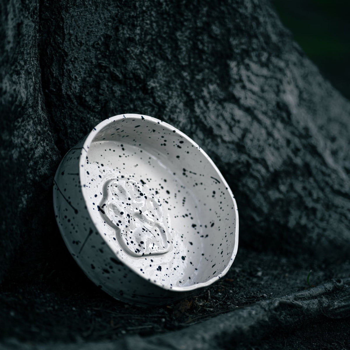 A speckled ceramic bowl resting against a tree trunk outdoors.