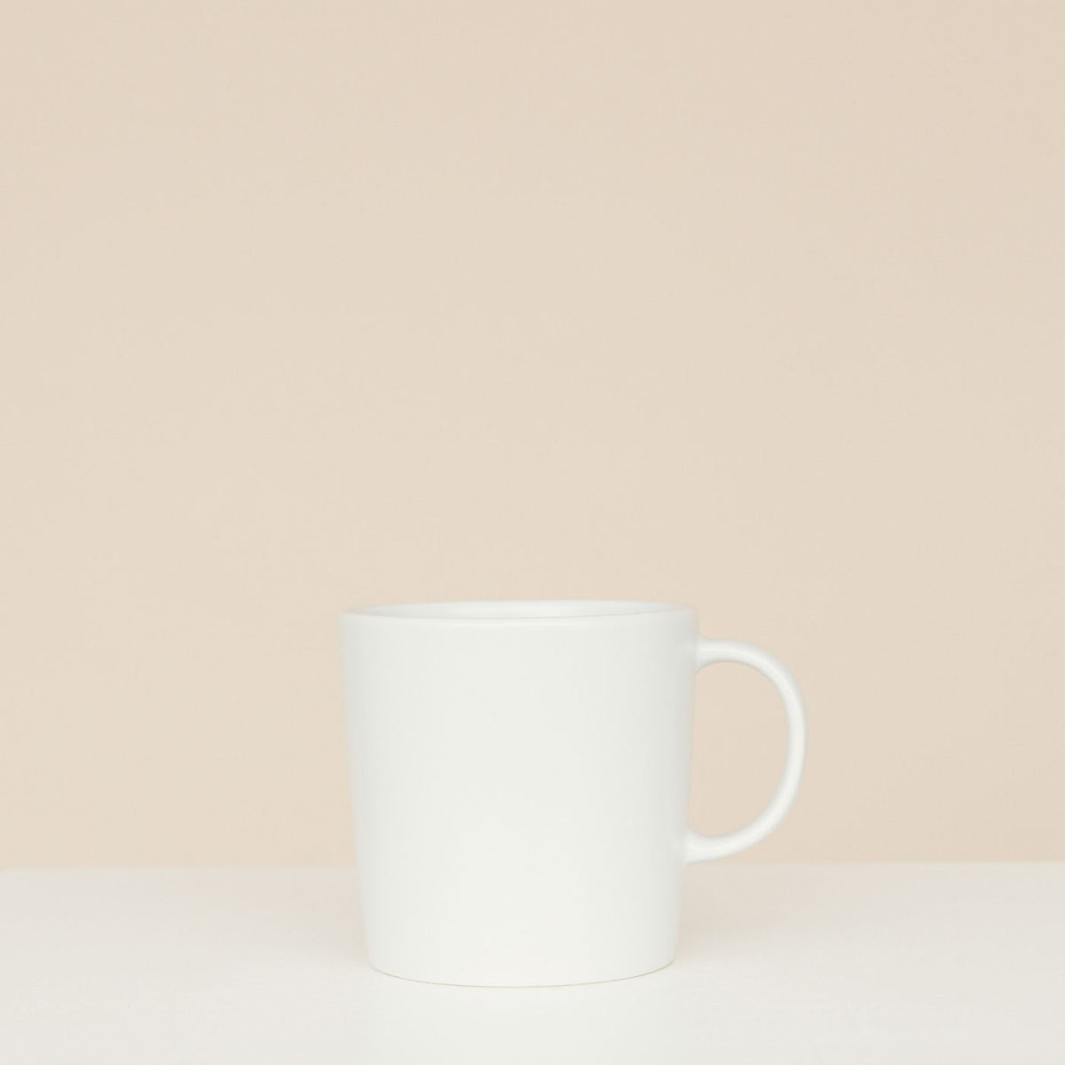 A simple white ceramic mug shown on a neutral beige background with nothing else in frame.